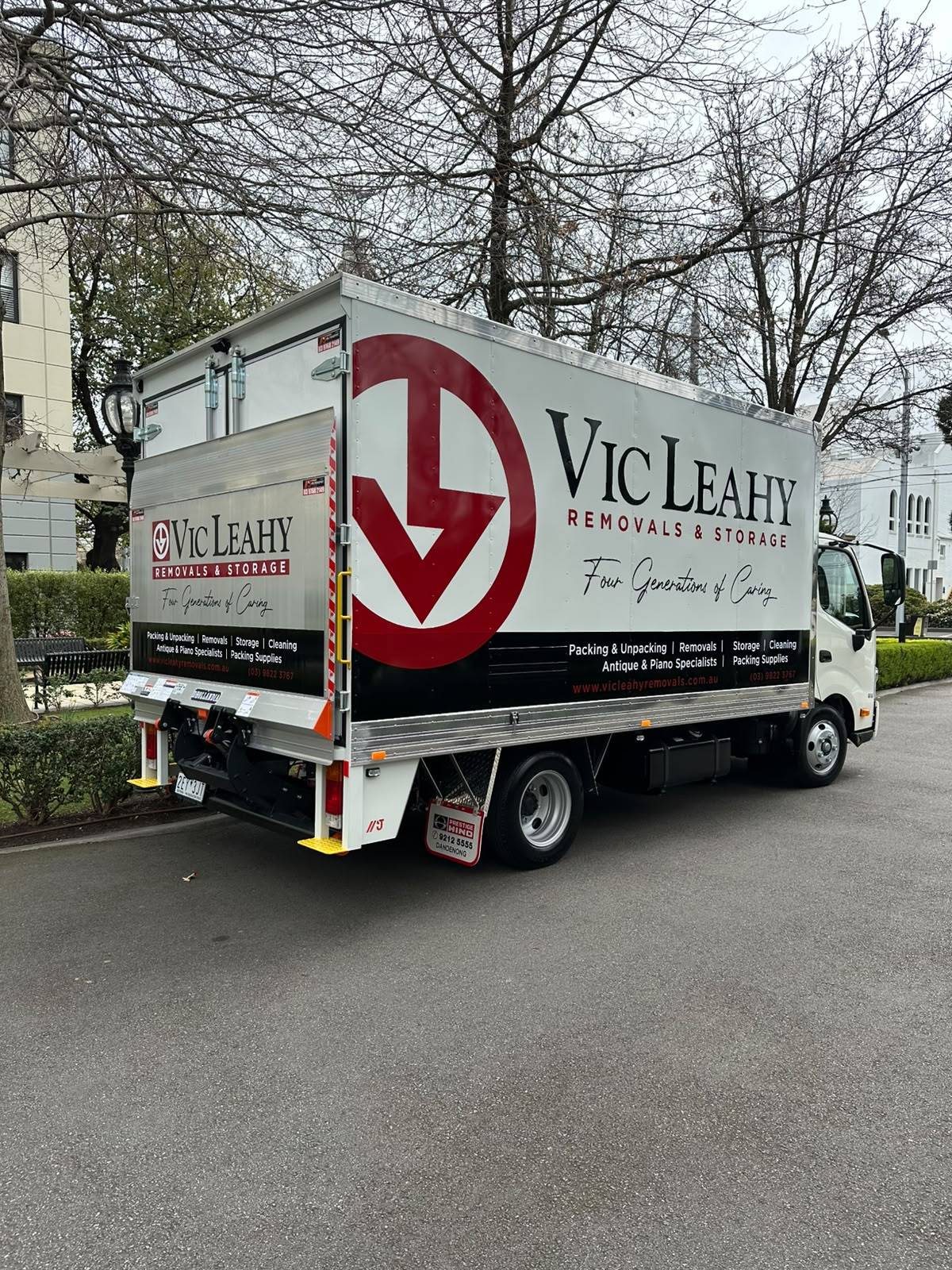 A Vic Leahy Removals and Storage truck with tail lift, parked on a leafy Melbourne street